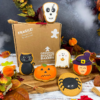 Hand-iced Halloween biscuits featuring a skull biscuit, black cat biscuit, pumpkin biscuit, ghost biscuit, spider biscuit and witch biscuit, displayed with Original Biscuit Bakers gift packaging in an autumn-inspired Halloween setting.