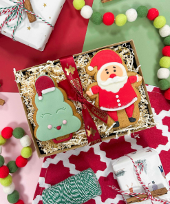Hand-iced Christmas biscuit gift box featuring Santa and Christmas tree biscuits, presented in a festive gift tray with red ribbon and seasonal decorations.