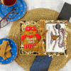 Gift box containing an Original Biscuit Bakers' “Super Dad” gingerbread biscuit and Billington’s gingerbread, presented with decorative straw on a woven placemat, styled with a mug, glasses, loose biscuits, and packaging.