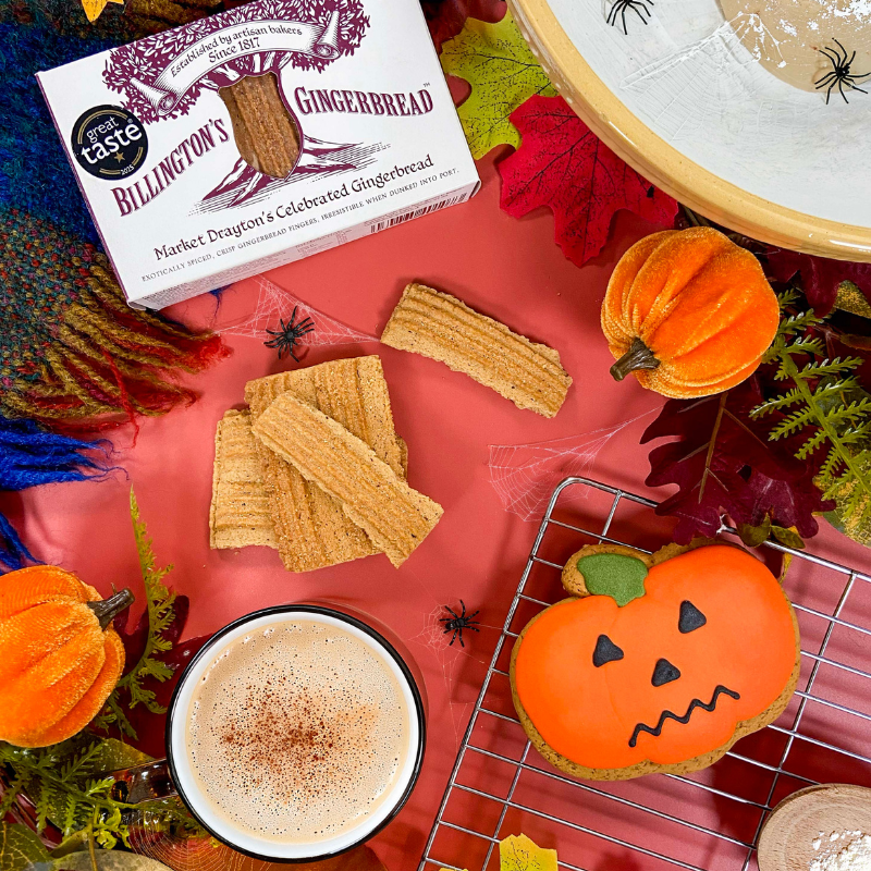 Billington's Gingerbread and an Original Biscuit Bakers pumpkin biscuit displayed in an autumn Halloween setting with a hot drink, seasonal pumpkins, autumn leaves, cobweb decorations and decorative spiders.