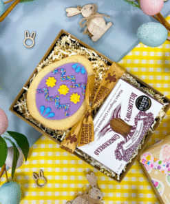 Easter-themed gift box featuring a hand‑iced purple sugar cookie egg alongside a pack of Billington’s Gingerbread fingers, displayed on yellow gingham with pastel Easter decorations.