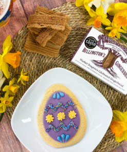 Original Biscuit Bakers Easter egg sugar cookie with colourful icing, displayed alongside Billington’s Gingerbread fingers and spring daffodils.