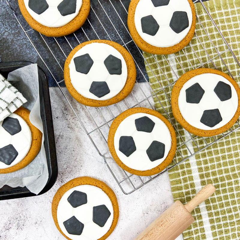 Freshly baked football‑design gingerbread biscuits by Original Biscuit Bakers on a wire rack, ideal for gift shops, sports merchandise, party bags, and seasonal retail.