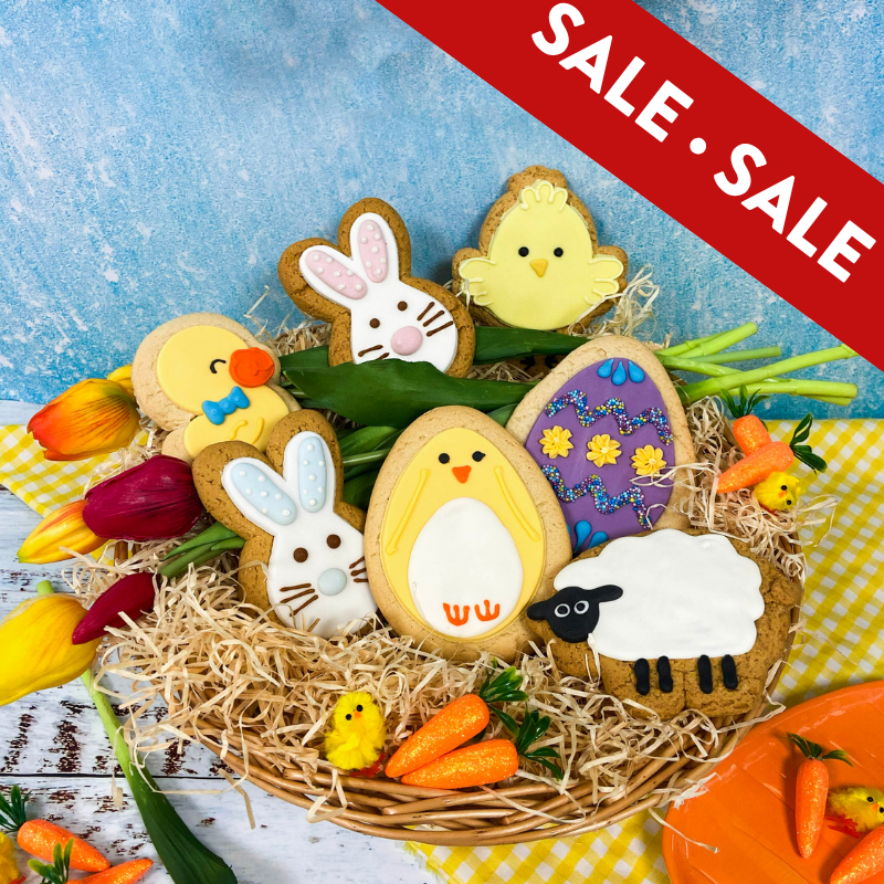 Easter‑themed decorated biscuits arranged in a basket with straw, featuring bunnies, chicks, a lamb and an Easter egg, surrounded by tulips and mini carrots, with a red ‘Sale’ banner across the corner.