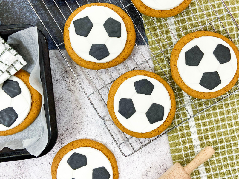 Freshly baked football‑design gingerbread biscuits by Original Biscuit Bakers on a wire rack, ideal for gift shops, sports merchandise, party bags, and seasonal retail.