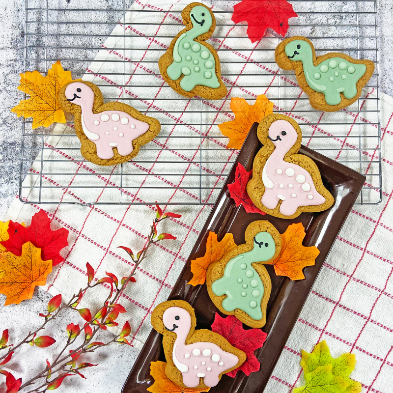Hand iced gingerbread dinosaurs pictured on a baking rack among autumn leaves.