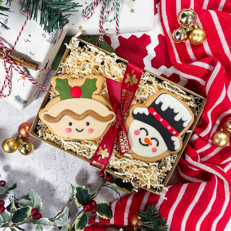 Christmas biscuit gift box featuring hand-iced sugar cookie mince pie and snowman biscuits, presented with festive ribbon and seasonal Christmas decorations.