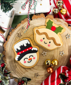 Hand-iced sugar cookie mince pie and snowman biscuits displayed on a rustic wooden serving board with festive Christmas decorations.